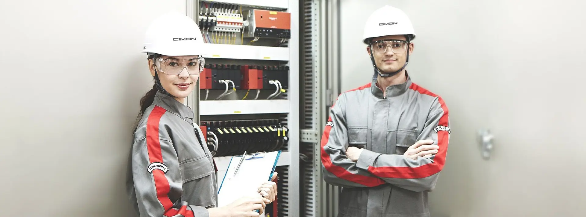 Two workers in CIMON apparel in front of a PLC rack