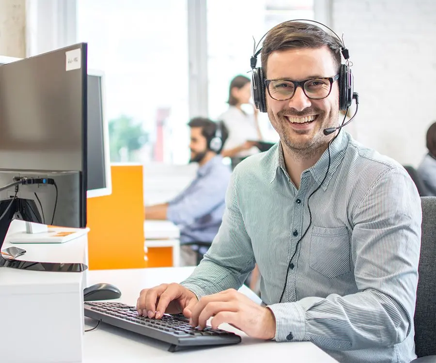 Person at desk smiling with a headset on in front of computer